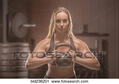 Stock Image - Caucasian woman lifting kettlebell in gymnasium. Fotosearch