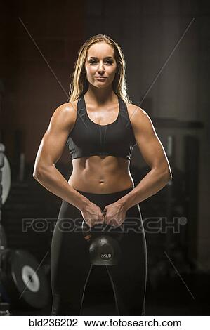 Stock Image - Caucasian woman lifting kettlebell in gymnasium. Fotosearch