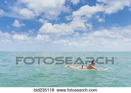Stock Photo - Caucasian woman paddling on surfboard in ocean. Fotosearch