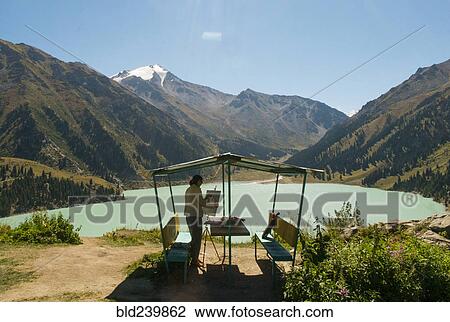 Stock Image - Caucasian woman painting mountain landscape. Fotosearch