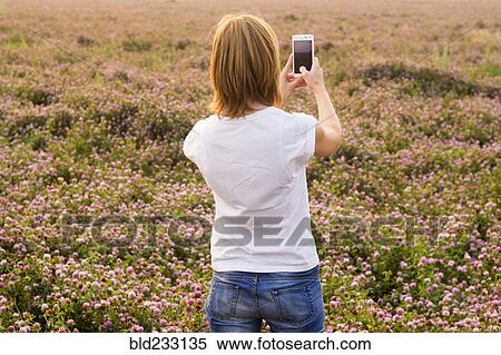 Stock Photography - Caucasian woman photographing field of flowers with cell phone. Fotosearch
