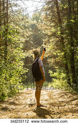 Stock Image - Caucasian woman photographing forest trees with cell phone. Fotosearch