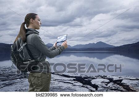 Stock Photography - Caucasian woman photographing mountain lake with digital tablet. Fotosearch