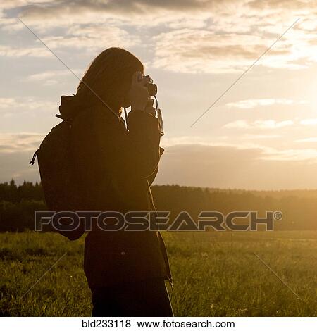 Caucasian woman photographing with camera in field at sunset View Large Photo Image Stock Photo - Caucasian woman photographing with camera in field at sunset. Fotosearch