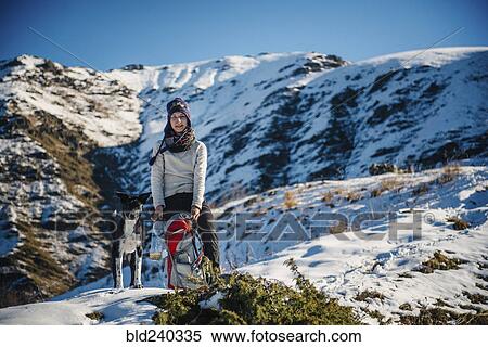 Stock Photography - Caucasian woman posing with dog and backpack on mountain. Fotosearch