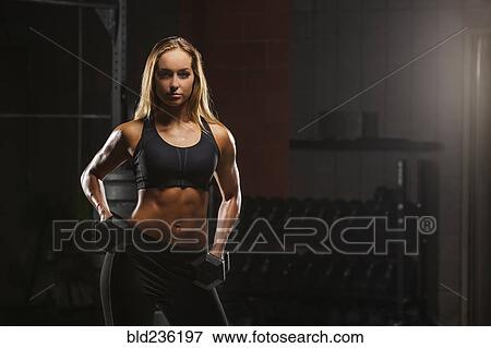 Stock Photo - Caucasian woman posing with dumbbells in gymnasium. Fotosearch