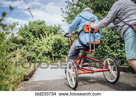Picture - Caucasian woman pushing daughter riding tricycle. Fotosearch