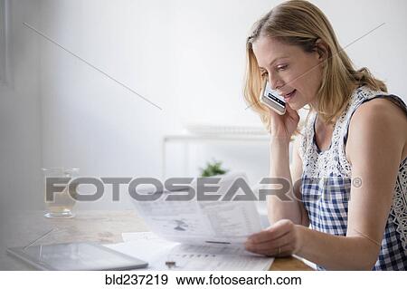 Stock Photo - Caucasian woman reading paperwork talking on cell phone. Fotosearch