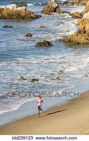 Stock Image - Caucasian woman running on beach. Fotosearch