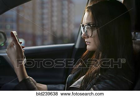 Stock Photo - Caucasian woman sitting in car texting on cell phone. Fotosearch