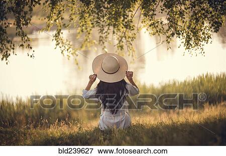 Caucasian woman sitting in grass near river holding hat View Large Photo Image Stock Photo - Caucasian woman sitting in grass near river holding hat. Fotosearch