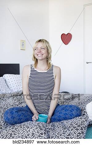 Caucasian woman sitting on bed drinking coffee View Large Photo Image Stock Photo - Caucasian woman sitting on bed drinking coffee. Fotosearch