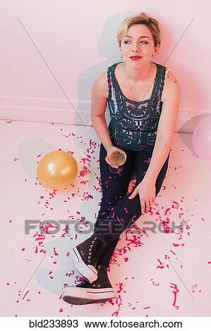 Stock Image - Caucasian woman sitting on floor at party covered in confetti. Fotosearch