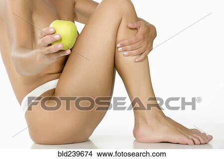 Picture - Caucasian woman sitting on floor showing green apple. Fotosearch
