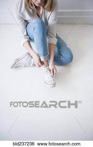 Caucasian woman sitting on floor tying shoelace View Large Photo Image Stock Photograph - Caucasian woman sitting on floor tying shoelace. Fotosearch