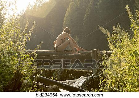 Picture - Caucasian woman sitting on log over waterfalls. Fotosearch