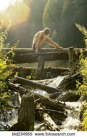 Stock Photography - Caucasian woman sitting on log over waterfalls. Fotosearch