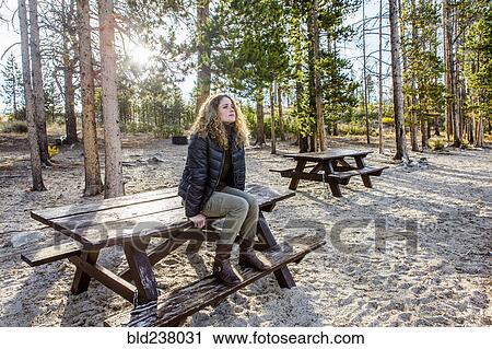 Stock Image - Caucasian woman sitting on picnic table. Fotosearch