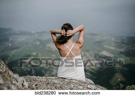 Stock Image - Caucasian woman sitting on rock overlooking landscape. Fotosearch