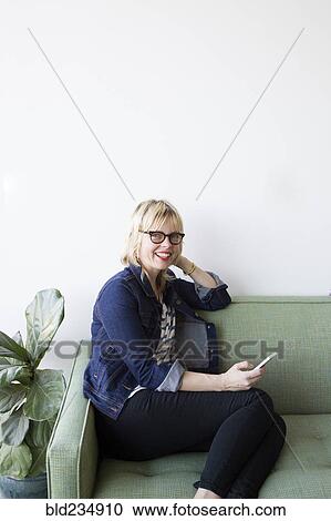 Stock Image - Caucasian woman sitting on sofa texting on cell phone. Fotosearch
