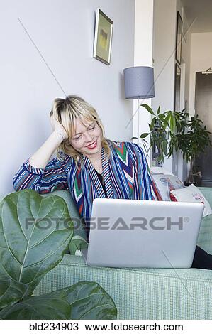 Stock Image - Caucasian woman sitting on sofa using laptop. Fotosearch