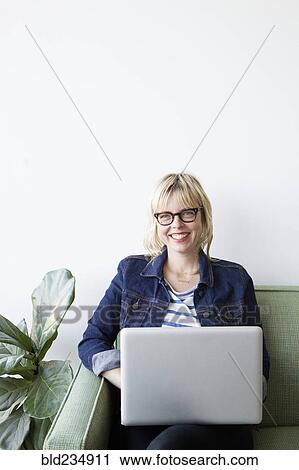 Stock Image - Caucasian woman sitting on sofa using laptop. Fotosearch