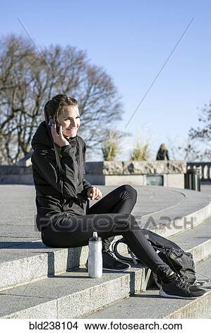 Picture - Caucasian woman sitting on staircase talking on cell phone. Fotosearch
