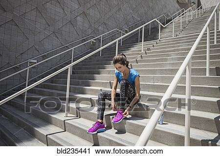 Stock Image - Caucasian woman sitting on staircase tying shoelace. Fotosearch