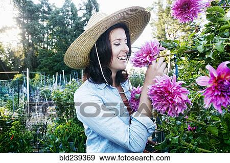 Stock Photo - Caucasian woman smelling flower in garden. Fotosearch