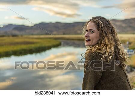Stock Image - Caucasian woman smiling near mountain river. Fotosearch