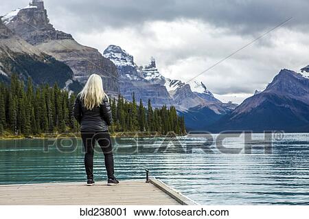 Stock Image - Caucasian woman standing at the end of dock on mountain lake. Fotosearch
