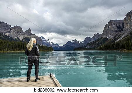 Stock Image - Caucasian woman standing at the end of dock on mountain lake. Fotosearch