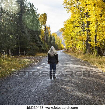 Stock Photo - Caucasian woman standing in road near trees. Fotosearch