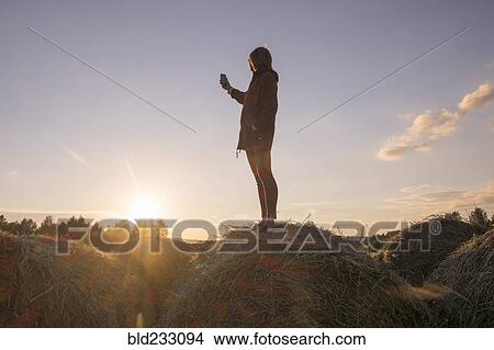 Picture - Caucasian woman standing on hay holding cell phone. Fotosearch