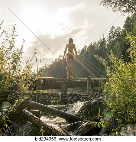 Stock Photograph - Caucasian woman standing on log over waterfalls. Fotosearch