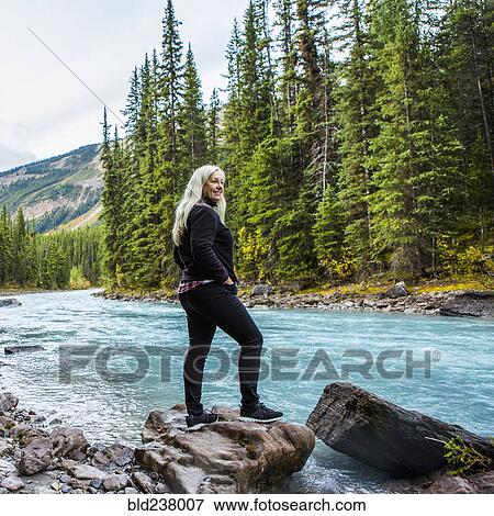 Stock Photo - Caucasian woman standing on rock near mountain river. Fotosearch