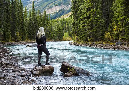 Stock Photograph - Caucasian woman standing on rock near mountain river. Fotosearch