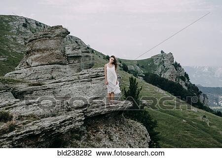 Stock Image - Caucasian woman standing on rock overlooking landscape. Fotosearch