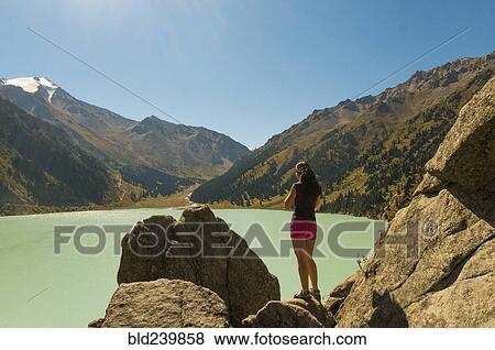 Stock Photo - Caucasian woman standing on rocks near mountain lake. Fotosearch