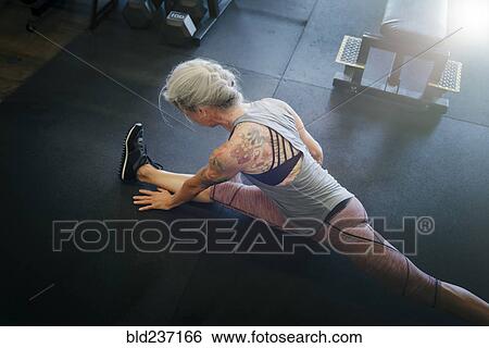 Caucasian woman stretching leg on gymnasium floor View Large Photo Image Stock Photograph - Caucasian woman stretching leg on gymnasium floor. Fotosearch