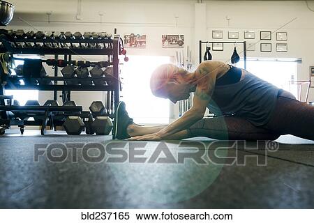 Stock Photography - Caucasian woman stretching leg on gymnasium floor. Fotosearch