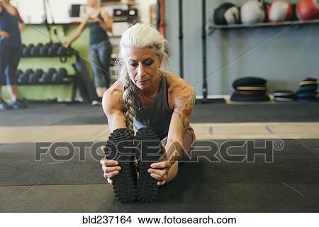 Picture - Caucasian woman stretching legs on gymnasium floor. Fotosearch
