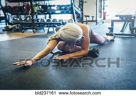 Stock Image - Caucasian woman stretching on gymnasium floor. Fotosearch