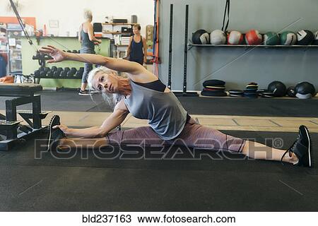 Stock Image - Caucasian woman stretching on gymnasium floor. Fotosearch