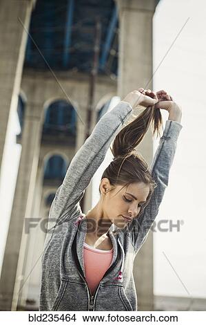 Picture - Caucasian woman stretching under overpass holding ponytail. Fotosearch
