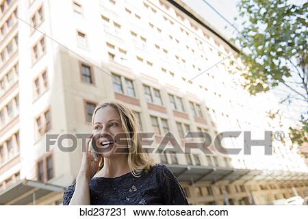Caucasian woman talking on cell phone in city View Large Photo Image Stock Image - Caucasian woman talking on cell phone in city. Fotosearch