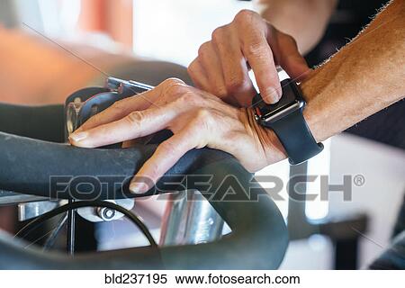 Stock Photography - Caucasian woman tapping smart watch on stationary bicycle. Fotosearch