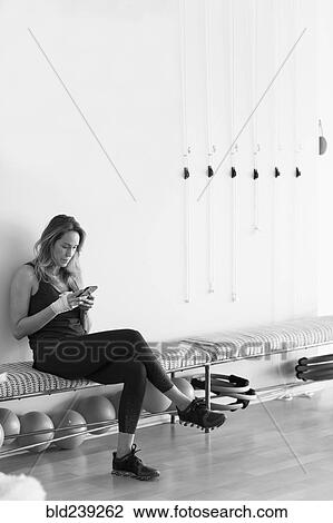 Stock Image - Caucasian woman texting on cell phone in gymnasium. Fotosearch