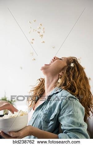 Stock Image - Caucasian woman throwing popcorn into mouth. Fotosearch