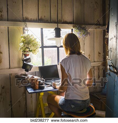 Stock Photo - Caucasian woman using laptop near rustic window. Fotosearch